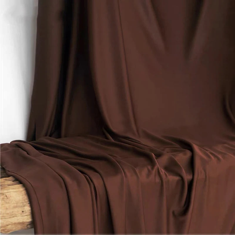 A close-up of rich brown stretch jersey fabric draped elegantly, showing soft folds and texture.