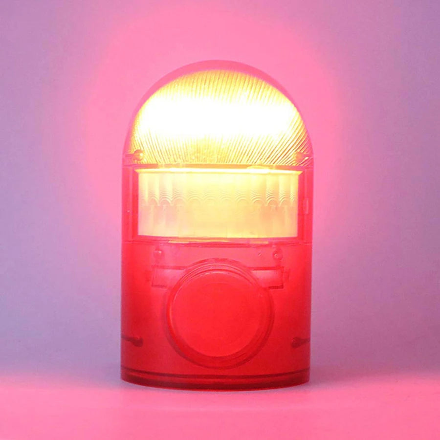 A red solar-powered motion sensor alarm with a clear dome and strobe light is shown against a pink background.