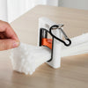 A hand holds a white cable tie organizer with a black carabiner clip, demonstrating its use for managing cables.