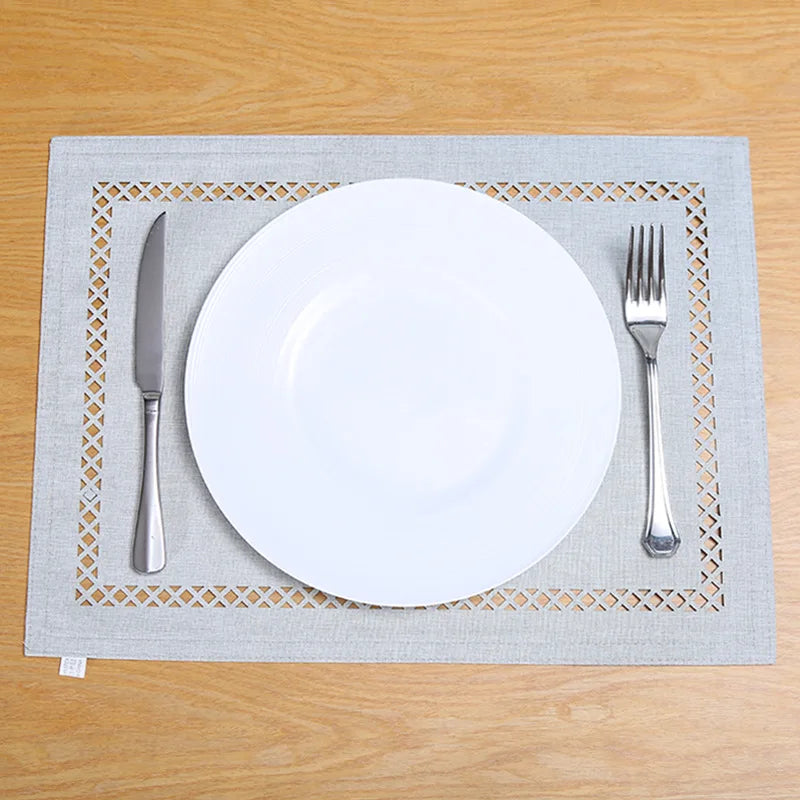 A white plate and silverware are placed on a gray linen placemat with a woven pattern on a wooden table.