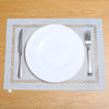 A white plate and silverware are placed on a gray linen placemat with a woven pattern on a wooden table.