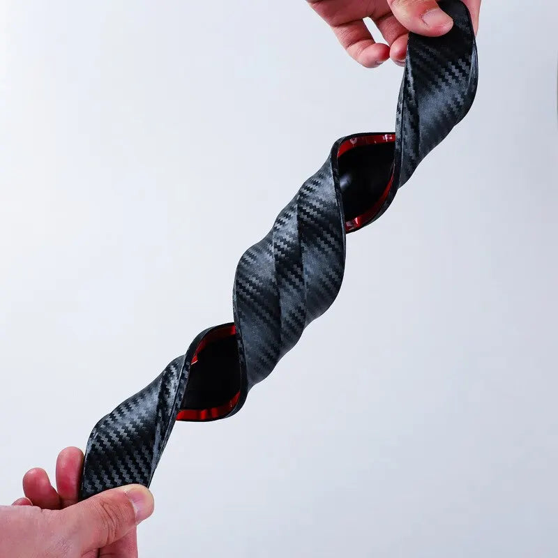 A hand holds a black carbon fiber anti-collision bumper protector strip, showing its woven texture and red accents.