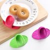 Pink silicone finger covers for baking and cooking resting on a wooden board with a plate of biscuits