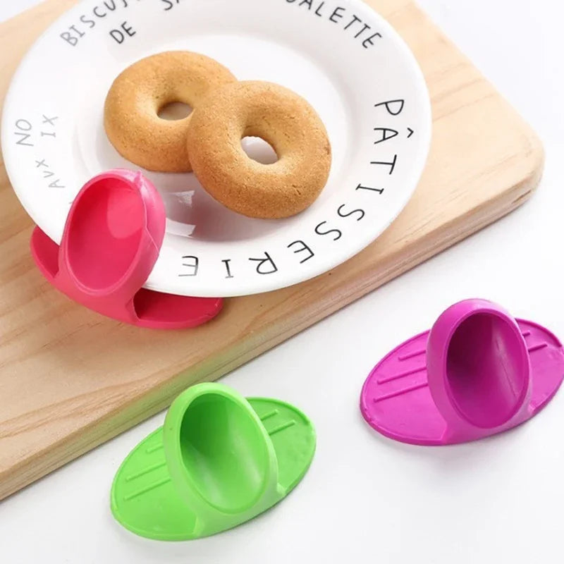 Pink silicone finger covers for baking and cooking resting on a wooden board with a plate of biscuits