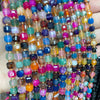 A close-up of multicolored natural stone square faceted beads in various shades of pink, blue, green, and amber.
