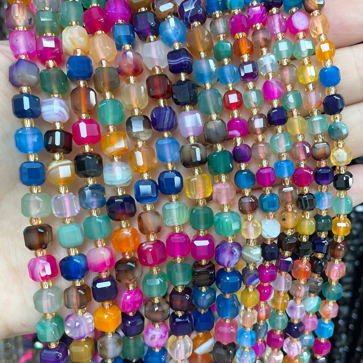 A close-up of multicolored natural stone square faceted beads in various shades of pink, blue, green, and amber.