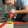 A man is using a rotary cleaning brush with an extension shaft on a drill to clean a rug.