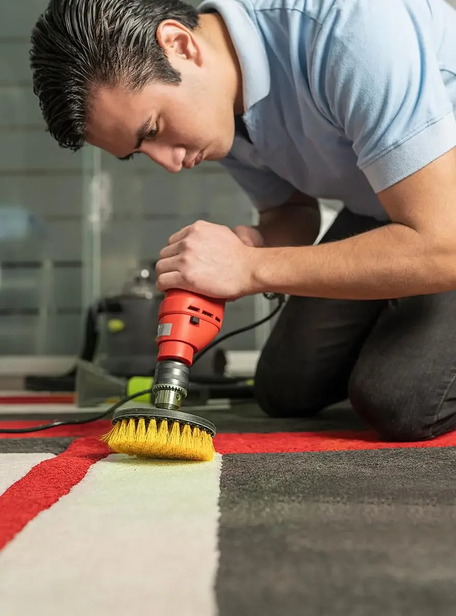 A man is using a rotary cleaning brush with an extension shaft on a drill to clean a rug.