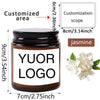 A dark brown glass jar candle with a black lid featuring custom logo text and jasmine flowers.