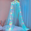A sheer blue mosquito net with LED lights draped over a bed for a canopy effect.