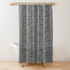 A black and white leopard print shower curtain hanging from a gold rod.