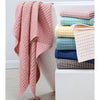 A stack of pink, light green, and blue waffle weave bath towels are displayed on a white shelf.