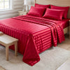 A vibrant red striped satin bed sheet set is displayed on a bed with light wood accents.