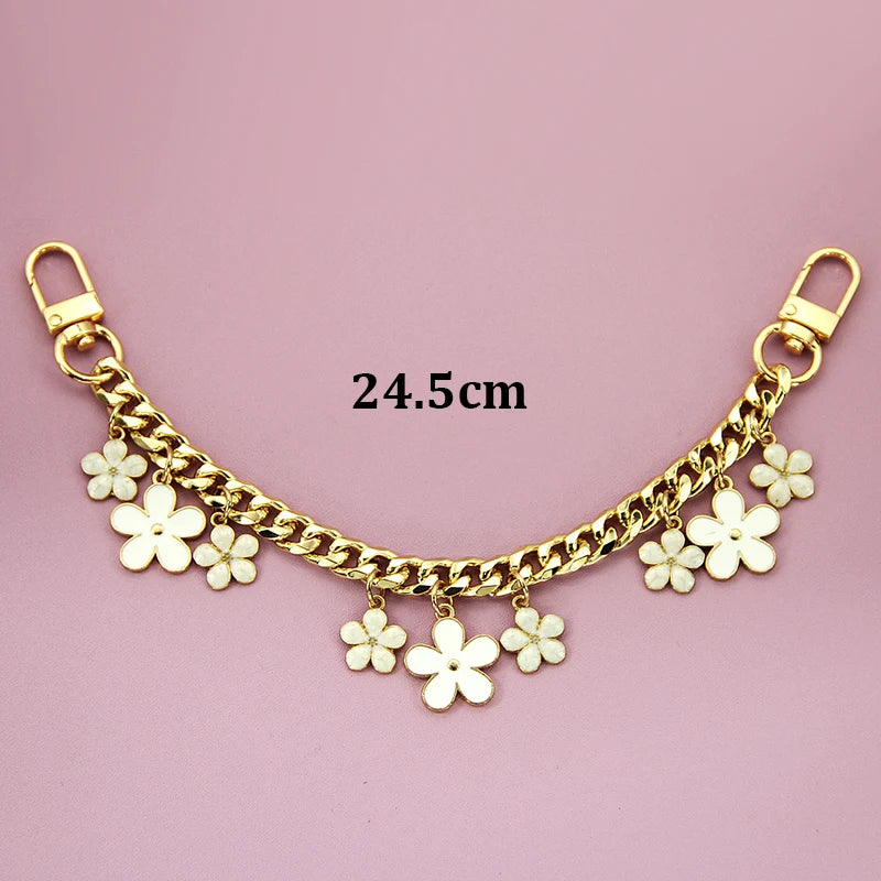 Gold chain phone strap featuring small white flower charms against a pink background.