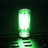 A glowing green glass accent LED night light resting on a dark green textured surface.