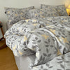 A gray duvet cover set featuring a soft print of olive green leaves and gold accents on a bed.