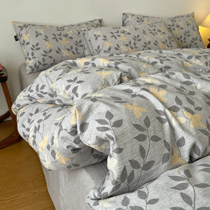A gray duvet cover set featuring a soft print of olive green leaves and gold accents on a bed.