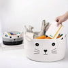 A hand is placing a white book into a woven cotton rope storage basket shaped like a cat face.