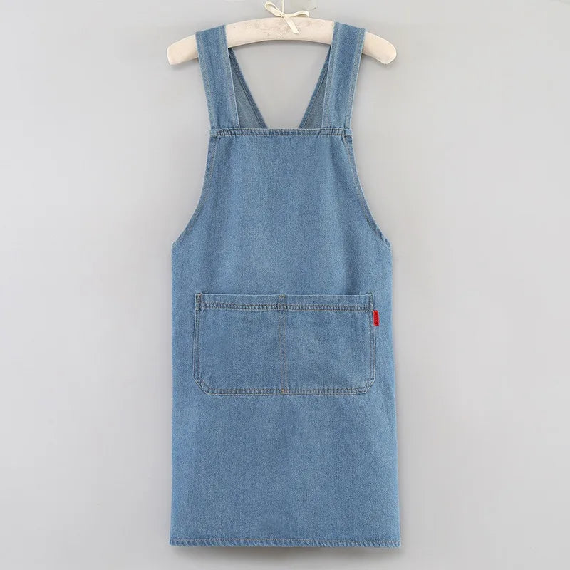A denim blue cross-back apron with chest pockets and a front pocket, displayed on a hanger.