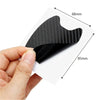 A hand holds a black carbon fiber car door handle protective cover, showing its texture and dimensions.