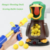 A hand holds a blue dart gun aiming at a green duck target game with yellow darts.