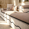 A beige striped chenille sofa cover with a pleated hem and black trim, displayed on a light-colored upholstered bed.