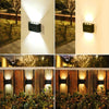 A solar powered outdoor wall light illuminating a pathway and surrounding foliage.
