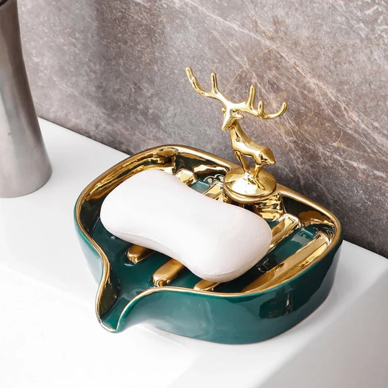 A green ceramic soap dish with a gold drain rack holding a white leaf-shaped ceramic soap bar.