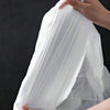 A hand is holding a large, white, thickened drawstring trash bag with handles.
