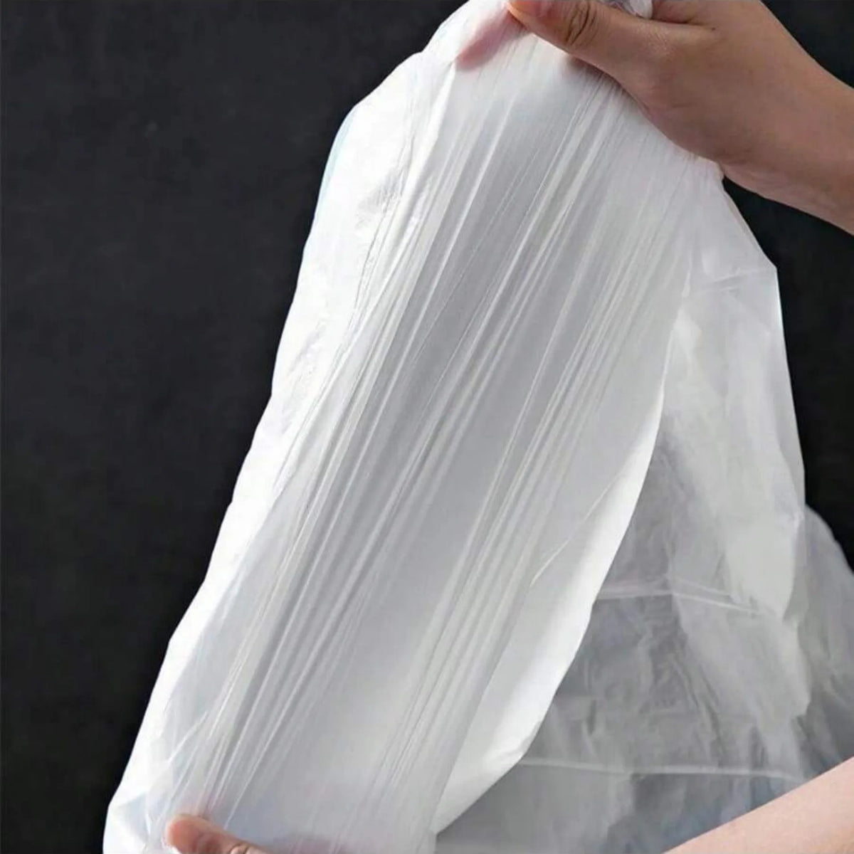 A hand is holding a large, white, thickened drawstring trash bag with handles.