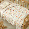 A white and floral patterned cotton gauze baby swaddle blanket draped over a wooden crib railing.