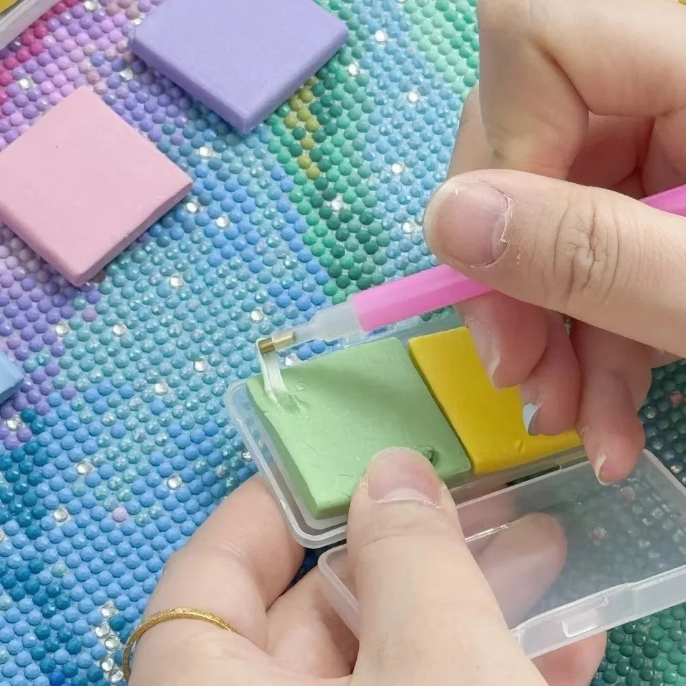 Hands are applying silicone diamond painting clay in various colors onto a grid surface.
