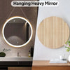 A round, illuminated mirror is hanging on a wall above a dark countertop.