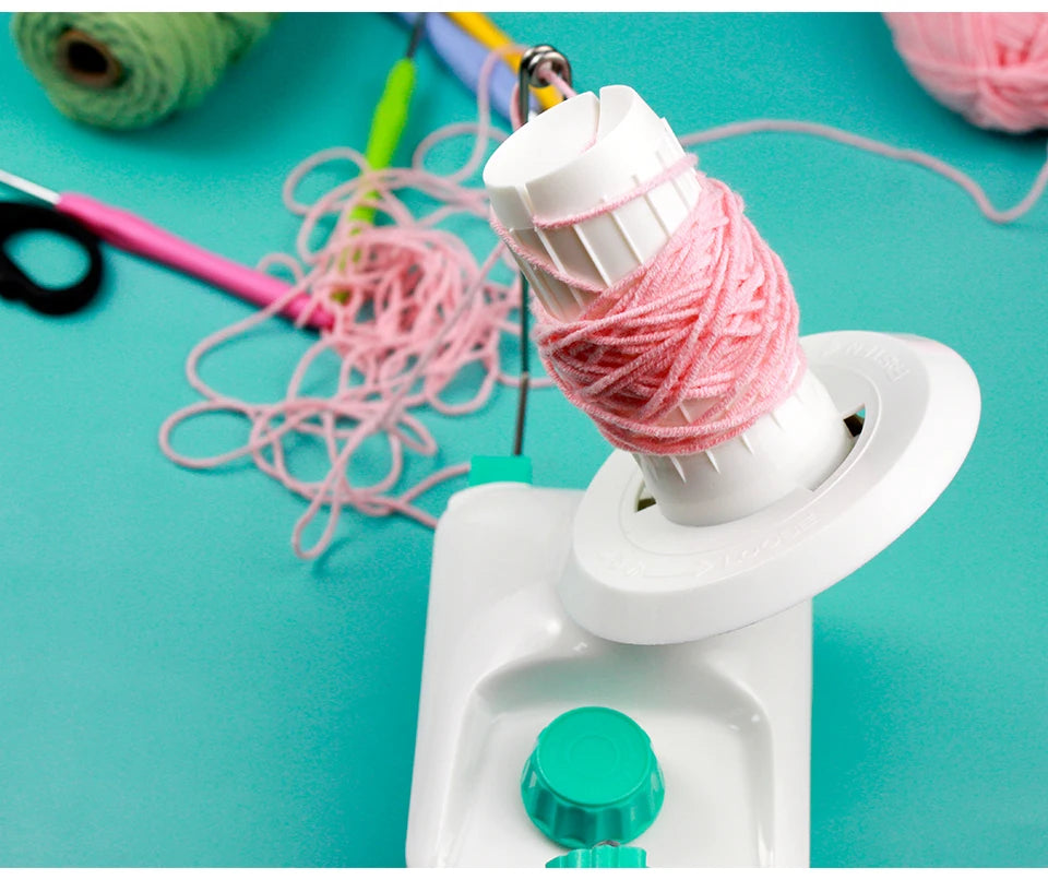 A white hand crank yarn winder is shown with pink yarn being wound onto it, set against a teal background.