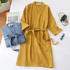 A mustard yellow lightweight cotton waffle robe hanging on a white surface next to a folded blue knitted garment.