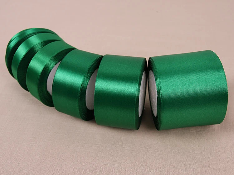 A roll of emerald green lustrous satin ribbon, shown in a row on a light background.