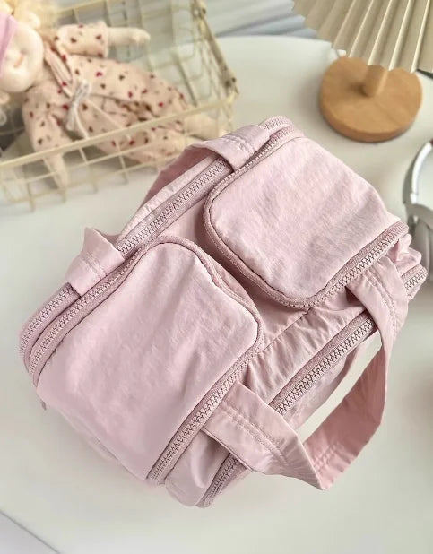 A light pink travel makeup bag with a wide opening is shown on a white surface.