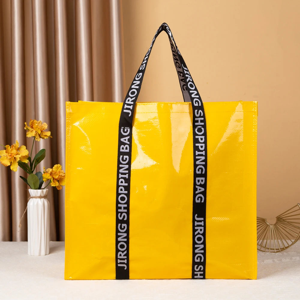 A bright yellow shopping bag with black straps is displayed against a beige background.