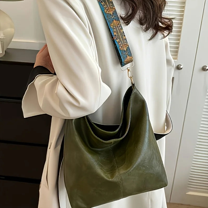 A woman holds a green leather shoulder bag with golden embroidery against a white coat.