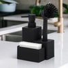 A black kitchen soap dispenser with a sponge holder and brush resting on a white countertop.