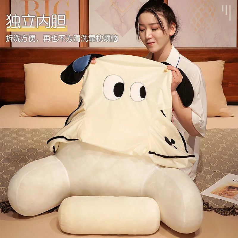 A person is holding a cream-colored plush cushion shaped like a cat and dog for use as a backrest on a bed.