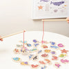 A wooden magnetic fishing game featuring various marine life shapes like fish, whale, and shark on a white surface.