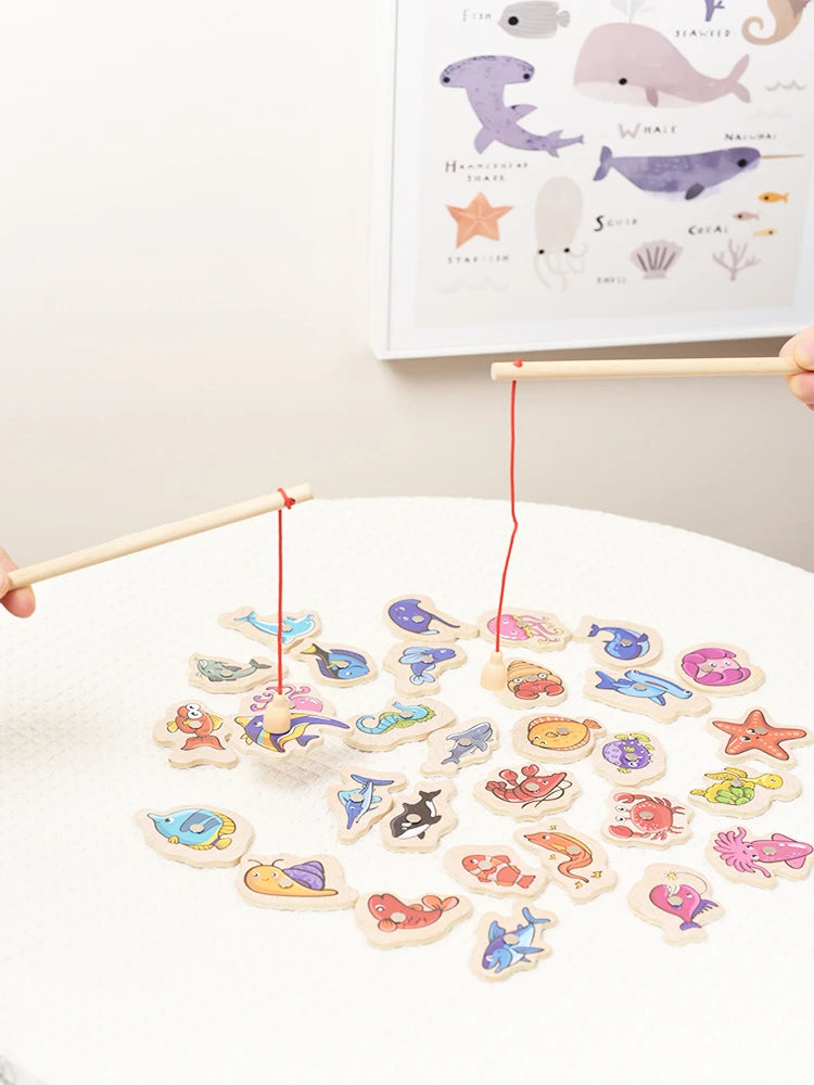 A wooden magnetic fishing game featuring various marine life shapes like fish, whale, and shark on a white surface.
