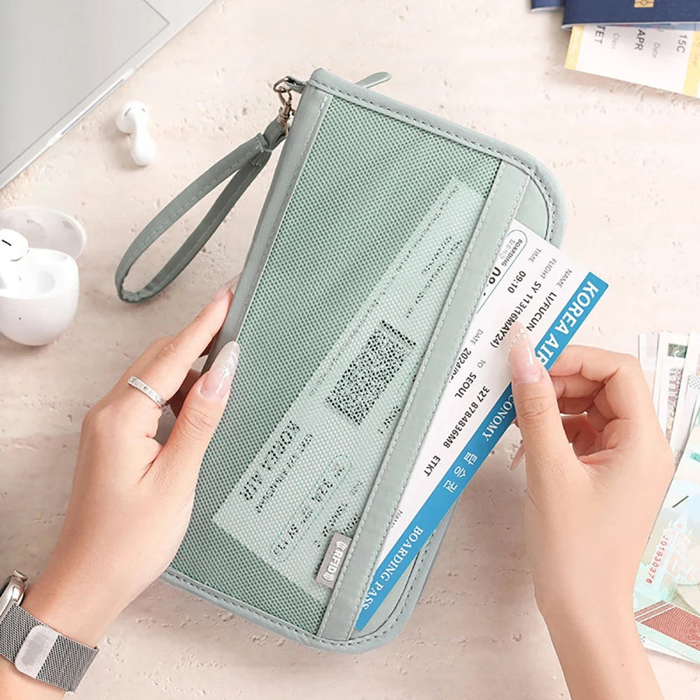 Una mano sostiene un portafolios de pasaporte verde claro con bloqueo RFID y una correa para la muñeca sobre una superficie c