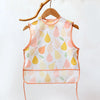 A sleeveless baby feeding bib with a watercolor pattern of pink and yellow pears, displayed on a wooden hanger.
