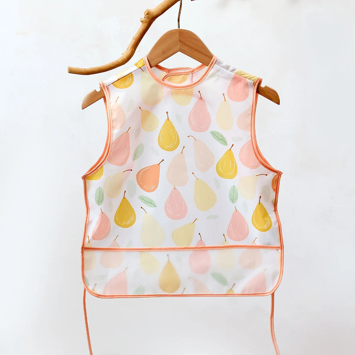 A sleeveless baby feeding bib with a watercolor pattern of pink and yellow pears, displayed on a wooden hanger.