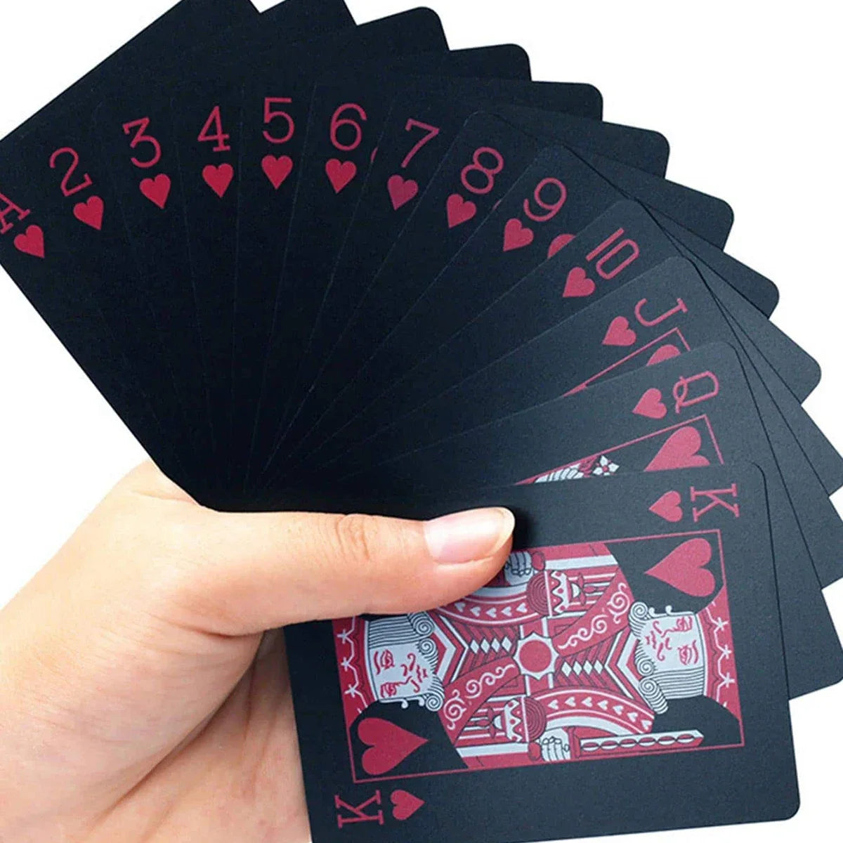 A hand holds a stack of black playing cards with red hearts, showing the numbered and face cards.