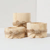 Three natural wooden cylindrical tea light holders tied with twine, used as mini flower pots.