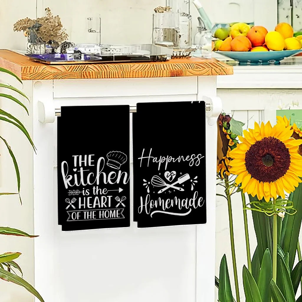 Two black kitchen towels featuring the slogan The kitchen is the heart of the home