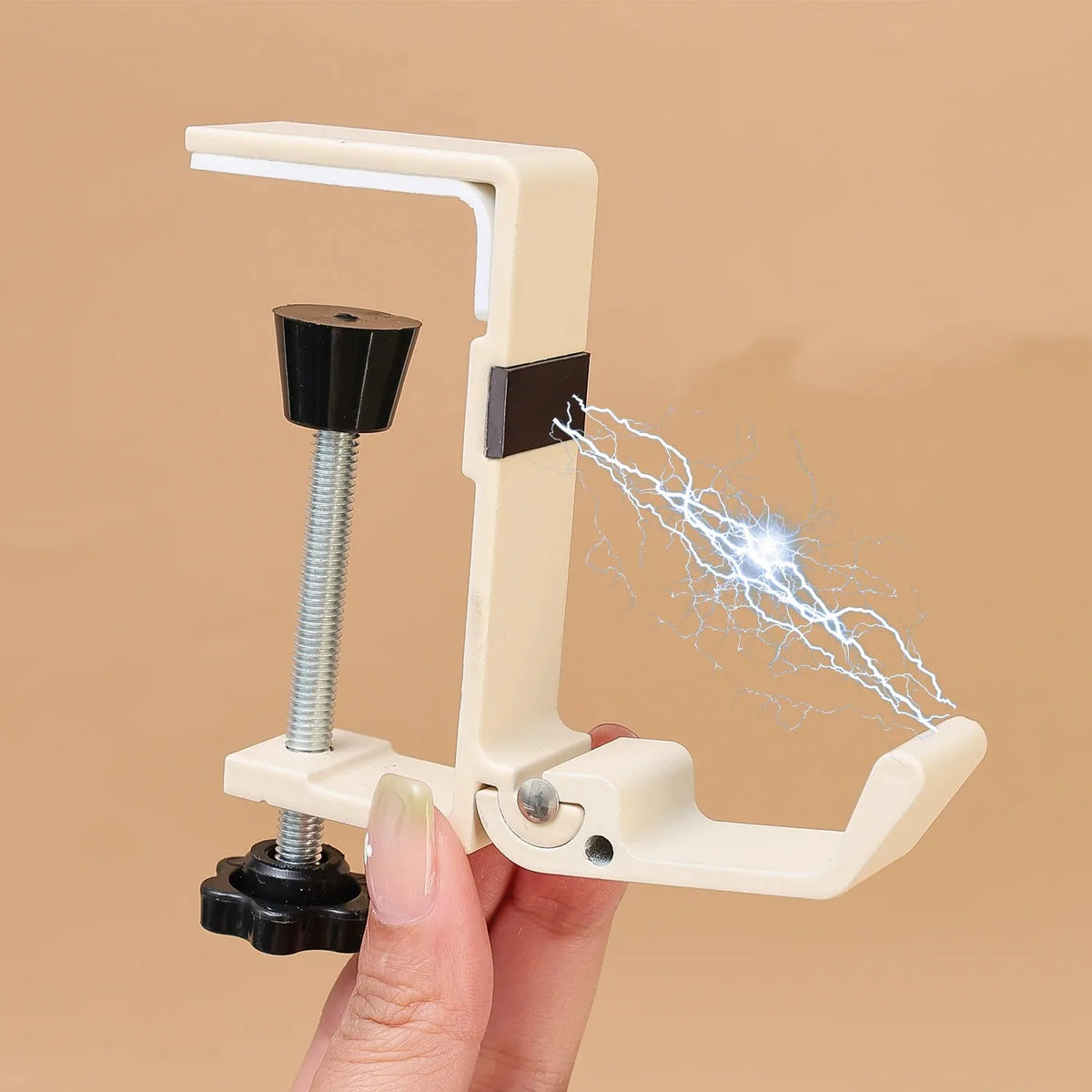 A hand holds a beige foldable aluminum desk hook device, demonstrating its function by shooting a small electrical spark.